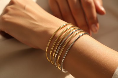 focus on a stylish woman's wrist, she is wearing thin rounded gold and silver bangle bracelets. lighting is warm and bright. 